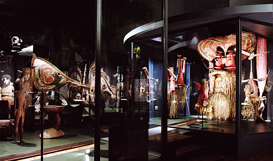 Ausstellungsansicht Masken der Südsee – Ein abgedunkelter Raum, darin Vitrinen, in denen Objekte der Ausstellungen Masken der Südsee unter spotlights gezeigt werden