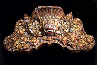 Hölzernes Brett mit Darstellung eines Dämonenkopfes (Boma), eingebettet in üppigen floralen Dekor