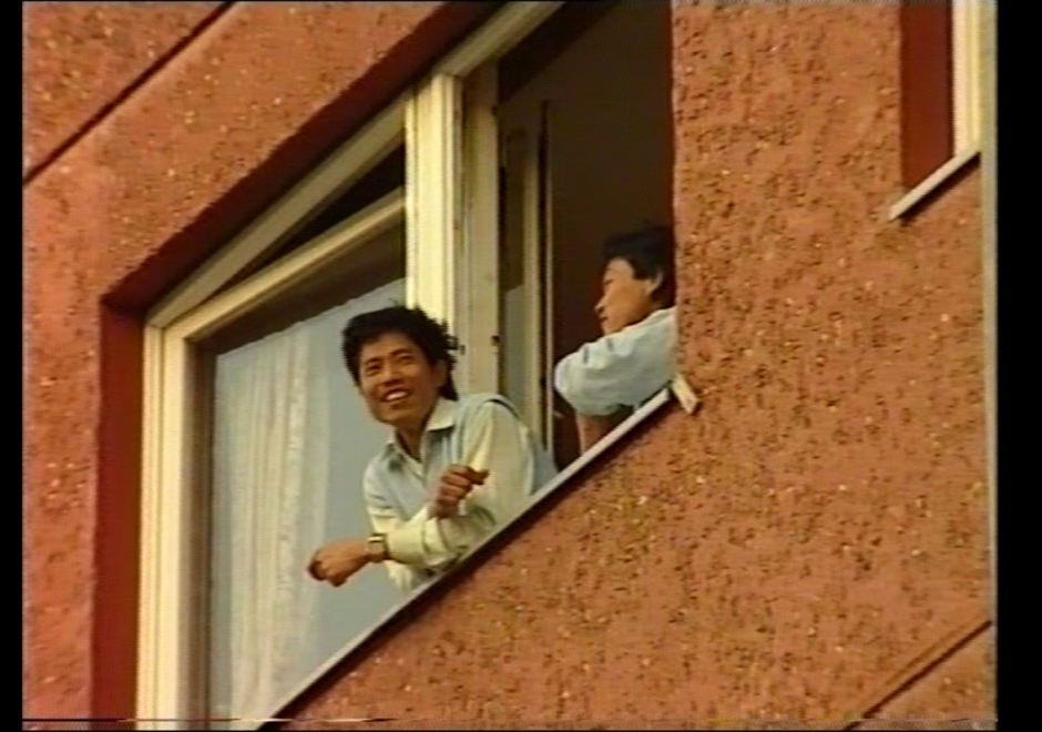 Zwei Personen gucken aus einem Fenster von einem Backsteinbau