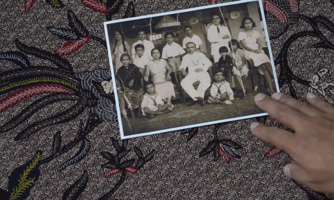 Still aus dem Film Love von Enang Wattimena – © Enang Wattimena Auf gebatiktem Stoff liegt ein schwarz-weißes Familienfoto, eine Hand berührt es